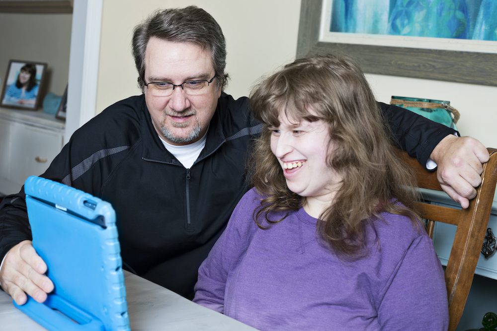 Father assists disabled daughter with her online homework via the digital tablet