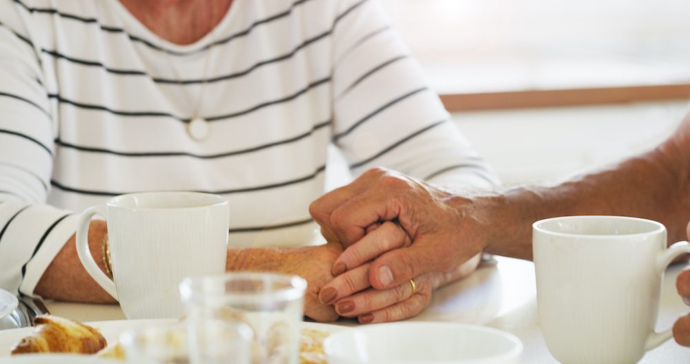 Cropped shot of a senior couple holding hands while having breakfast together at home