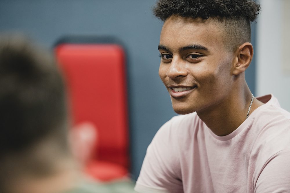 Two teenage boys are having a discussion while sitting in a classroom lesson at school.