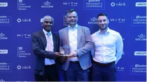 Three men posing with a glass award in front of a branded poster